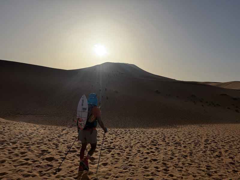 太陽に向かって砂丘を登るランナー